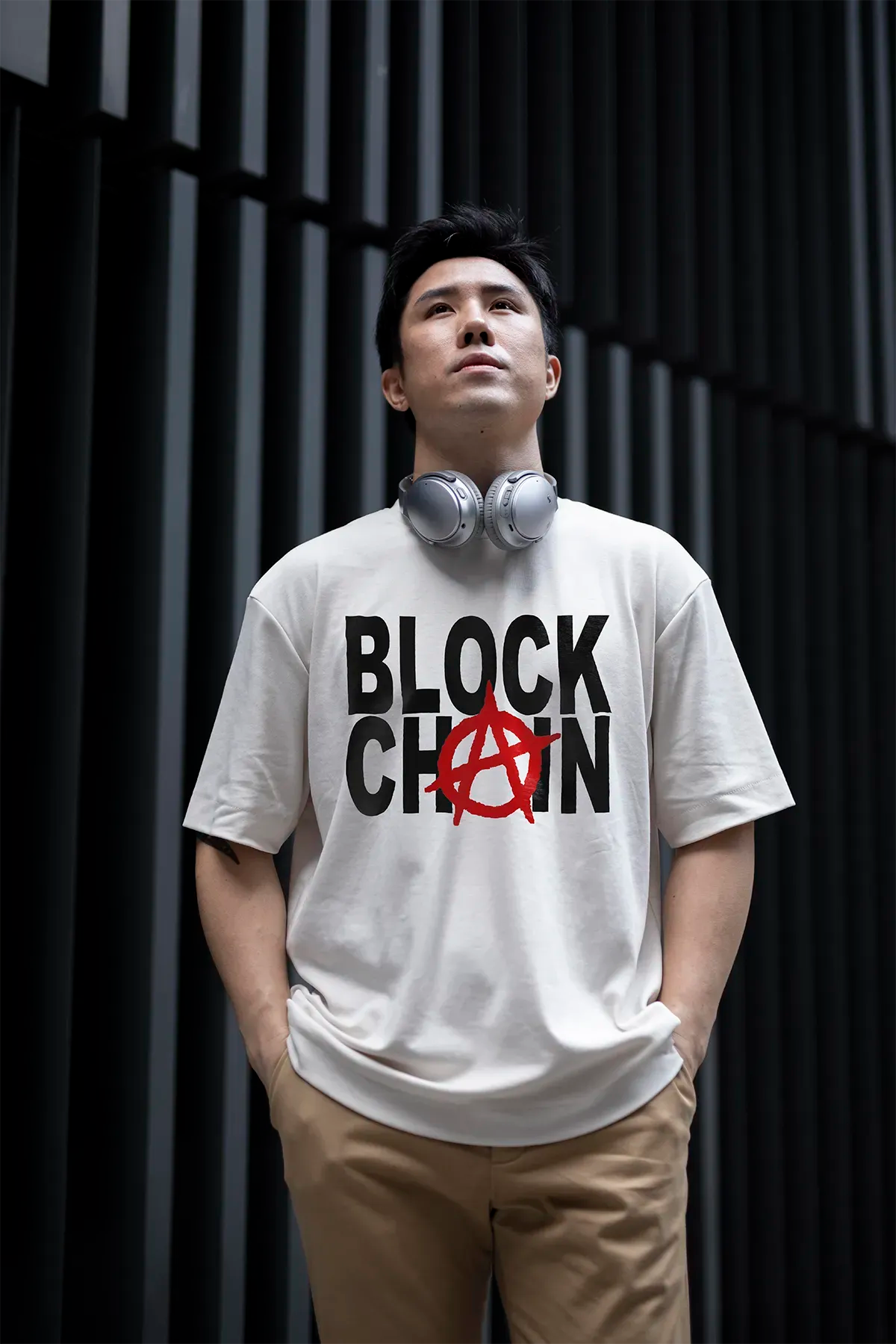 Streetwear T-Shirt with bold BLOCKCHAIN print and anarchy symbol, worn by an Asian male model in urban setting