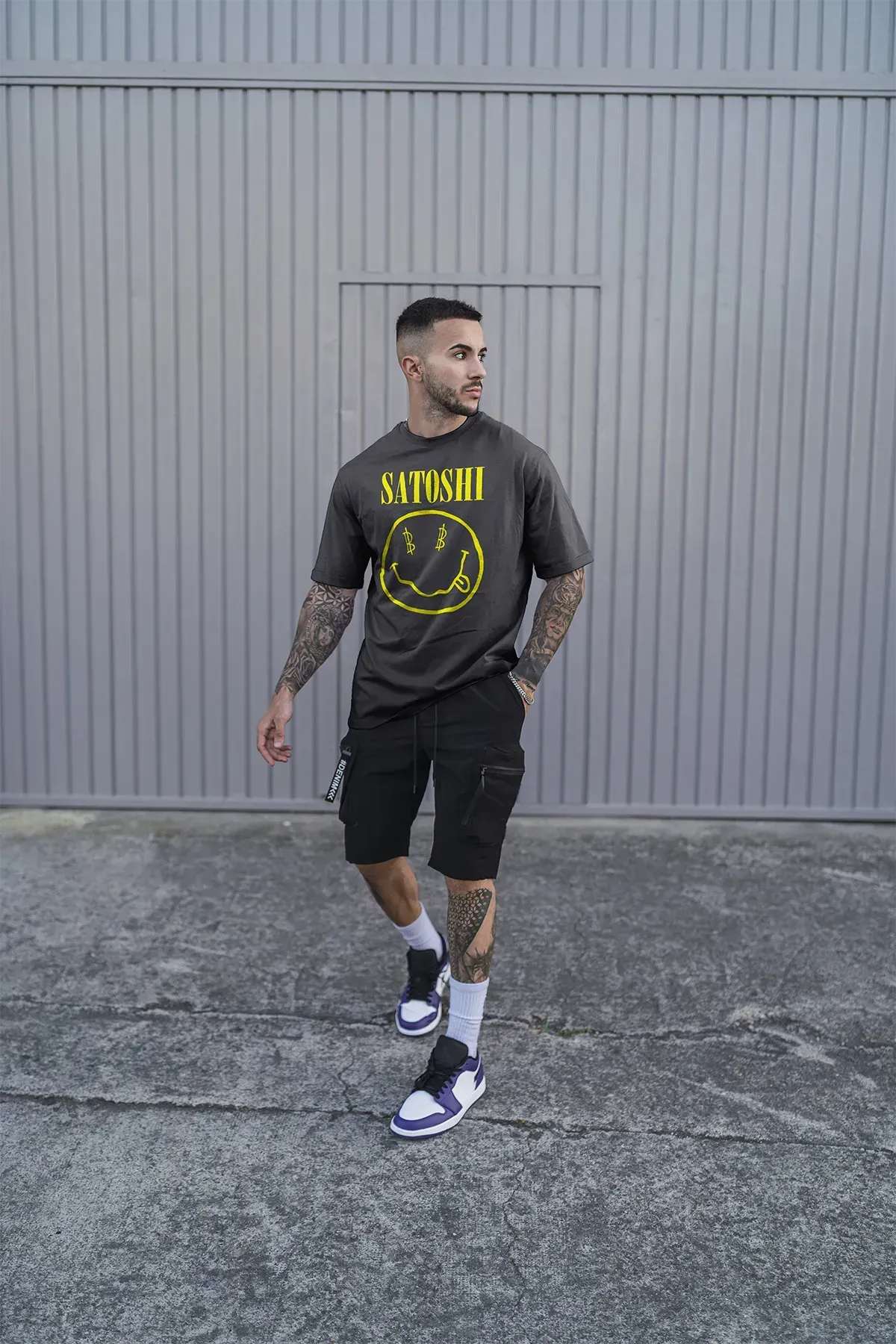 Streetwear T-Shirt with yellow SATOSHI print and cryptic smiley, worn by tattooed male model